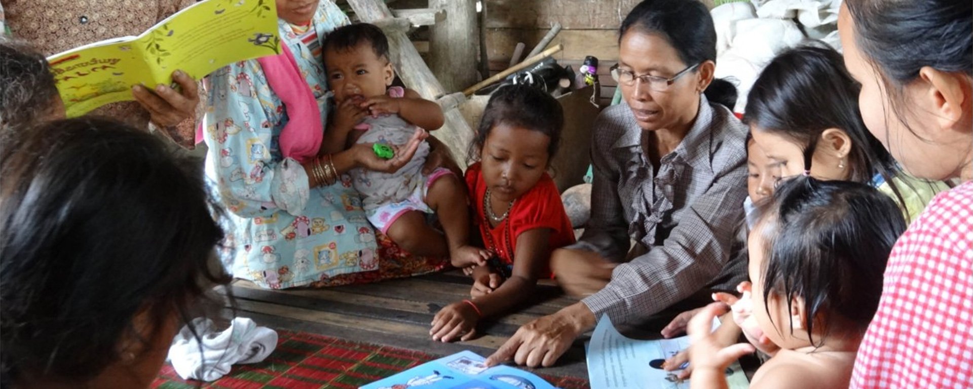 Adult teaching a group of children to read their first book